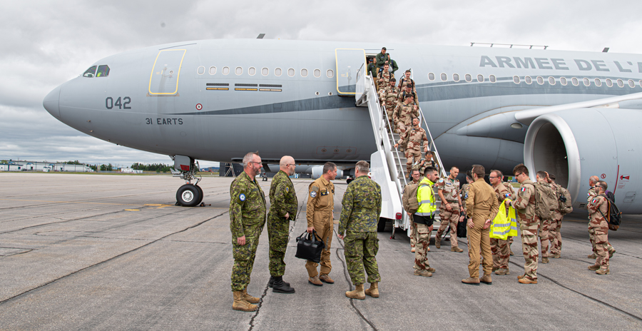 RCAF members greet French Air Force members as they descend the steps from a large grey military aircraft.