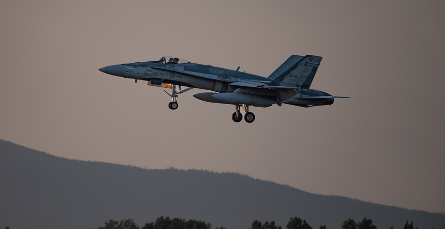 An RCAF fighter jet with its landing gear lowered ready to touch down at dusk.