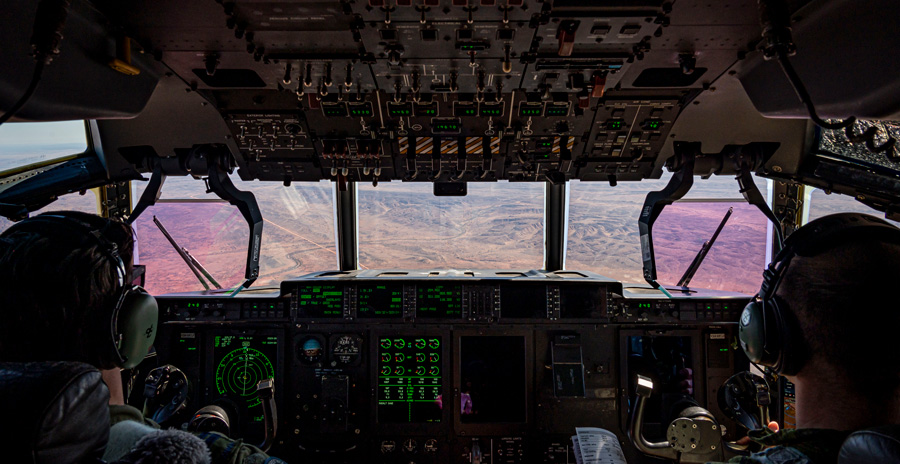 Cockpit view of a large military aircraft in flight with two pilots seated at the controls