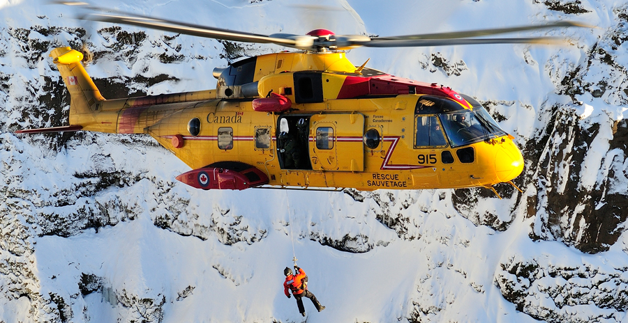 Rescue helicopter hoists a rescuer over snowy cliffs during a training exercise.