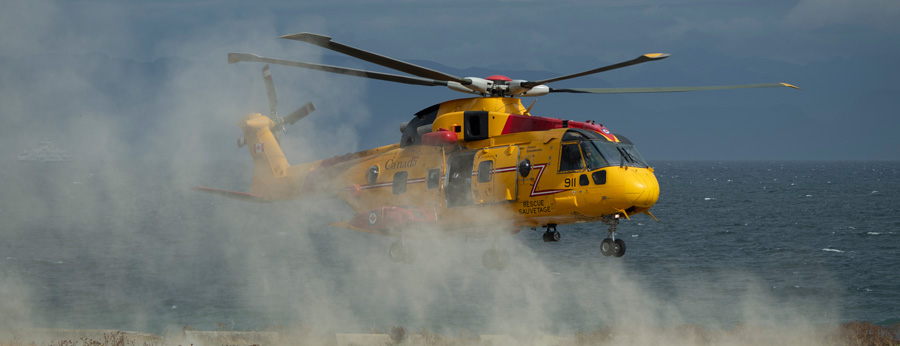 A yellow and red search and rescue helicopter landing on a sandy beach with the ocean in the background. 