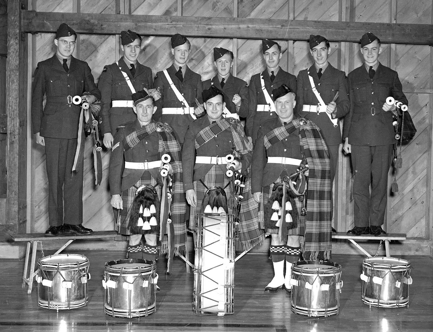 “The young pilots it produces for the Royal Canadian Air Force is one source of pride at No. 9 Service Flying Training School, Centralia, Ontario, but the station is also rightly proud of its pipe band. The organization at present comprises five drummers and seven pipers under the direction of Pipe Major, Corporal James Ross of London, Ontario, who has been playing the pipes for 15 years. President of the pipe band is Flying Officer C.A. Finley of Meaford, Ontario, and Warrant Officer Class 1 G.D. Taylor of Toronto is the secretary. In this picture are shown (in the front row from left to right) Pipe Major Corporal J. Ross, London, Ontario; Aircraftman Second Class K.A. Stuebing, Kitchener, Ontario; Aircraftman Second Class W.J. Mutch, Clinton, Ontario; (back row) Aircraftman Second Class L.J. Hutchison, Thamesford, Ontario; Aircraftman Second Class W.S. Stewart, Winnipeg, Aircraftman Second Class J. Graham, Winnipeg,; Aircraftman Second Class A.I. Russell, Winnipeg, Aircraftman Second Class J.S. Gair, Winnipeg,; Leading Aircraftman G. Fairlie, Windsor, Ont.; and Aircraftman Second Class H.A. Forgie, Winnipeg. Missing from the picture are Aircraftman Second Class T.A. Simpson, Winnipeg; and Leading Aircraftman H. Ince, Charlottetown, Prince Edward Island.” PHOTO: PL-14598, DND Archives
