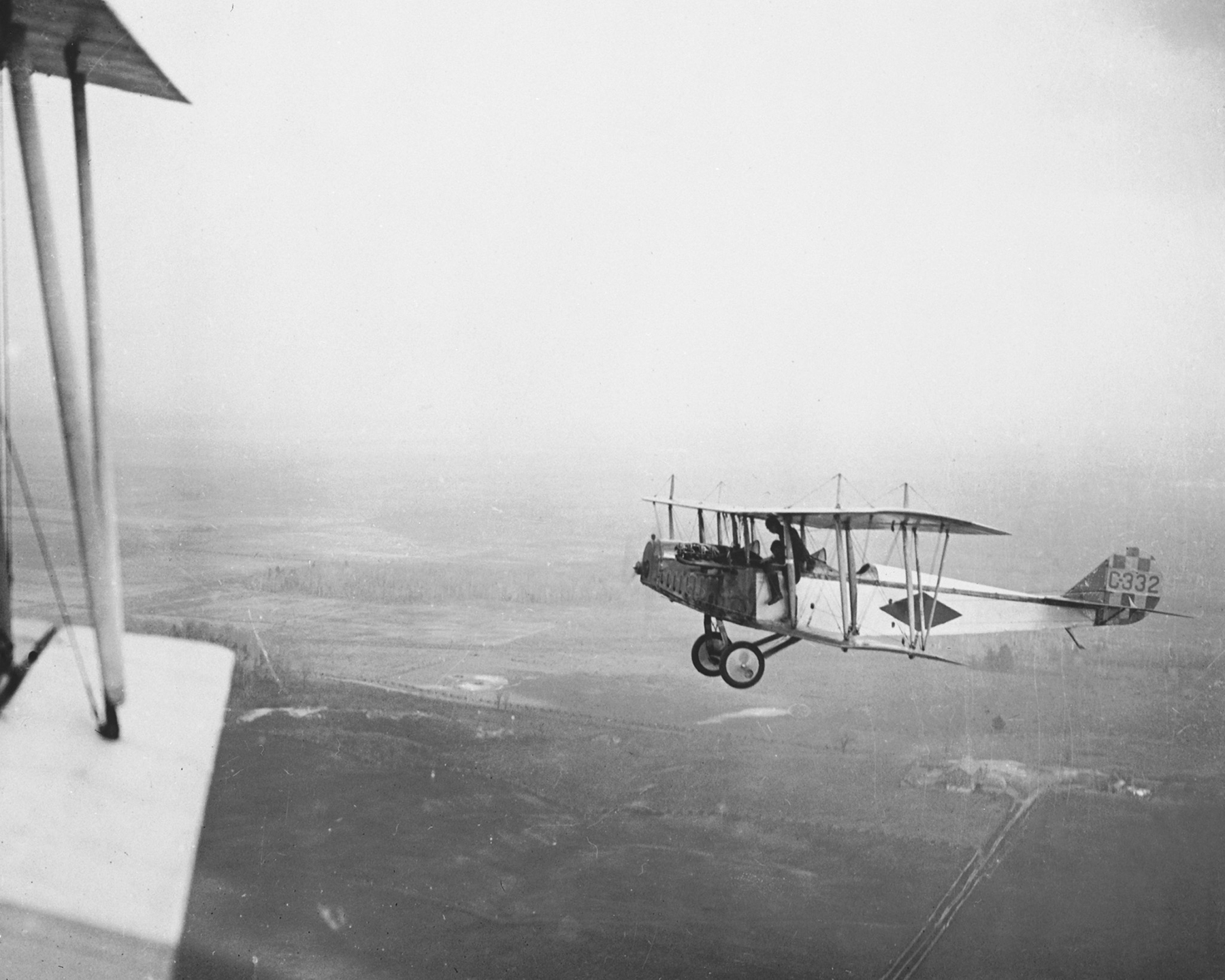 Two Royal Flying Corps Canada airmen, one having climbed out of his seat to straddle the side of the forward cockpit, chat about stability while in flight in their Curtiss JN-4 “Canuck” trainer – No. C332.  PHOTO: DND Archives, RE-19067-9