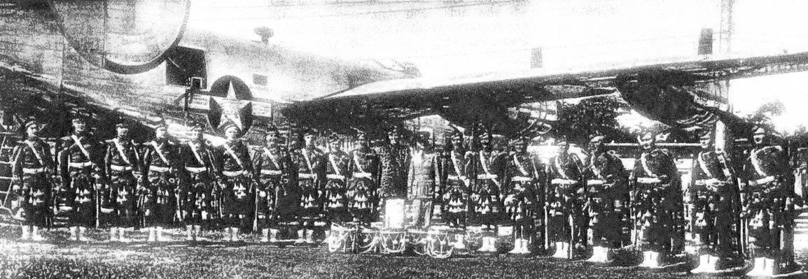 Members of the Royal Canadian Air Force Pipe Band gather beside a Boeing B-17 Flying Fortress while on a visit to Detroit, Michigan, during the Second World War. From left are James Ross (London, Ontario); Frank MacKenzie (Lucknow, Ontario); Jim Murphy (St. Catharines, Ontario); Les Hutchinson (Ingersoll, Ontario); unidentified piper, Biff Andrews (Clinton Ontario); Bert Ross (London Ontario); Jack Graham, Sandy Russell, Jack Gair, and Weary Wile (all from Winnipeg, Manitoba); Flying Officer Herbertson (Toronto, Ontario); Wally Simpson (Winnipeg, Manitoba); George Fairlie (Windsor, Ontario); Ken Stuebing (Kitchener, Ontario); Donald Fletcher (Lachute, Québec); Bill Mutch (Clinton, Ontario); Jack Smithson (Kitchener, Ontario); Harry Forgie (Winnipeg, Manitoba); and Tom Carroll (Kitchener, Ontario).