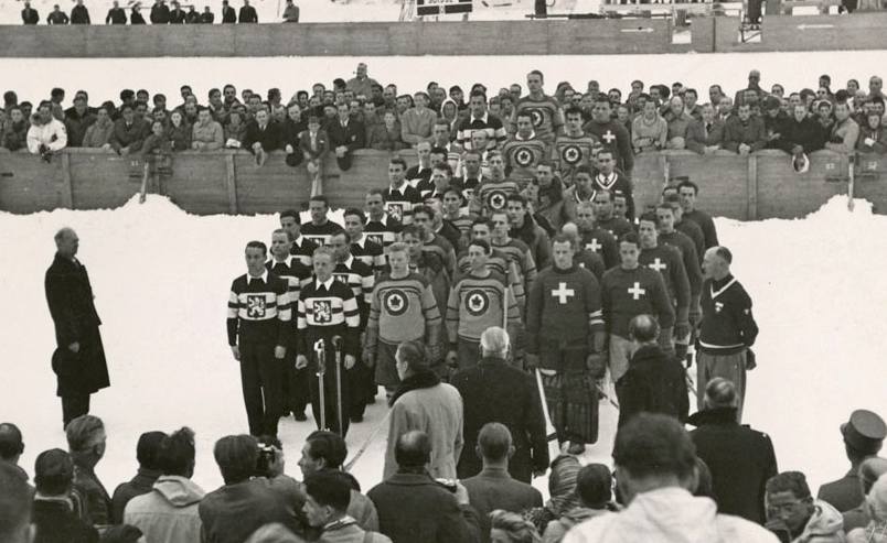 Three hockey teams stand in a close group outdoors with spectators around them. 