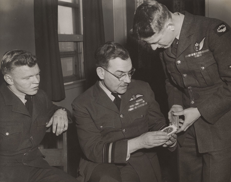 The RCAF Flyers' Roy Forbes shows his Olympic ice hockey gold medal to Air Marshal Wilf Curtis, Chief of the Air Staff, on April 7, 1948, while Orval "Red" Gravelle looks on. Note bomber wing on Forbes’ uniform. Air Marshal Curtis was a keen hockey fan and immediately supported the idea of sending an RCAF team to compete in the 1948 Winter Olympics. PHOTO: LAC MIKAN no. 4842101