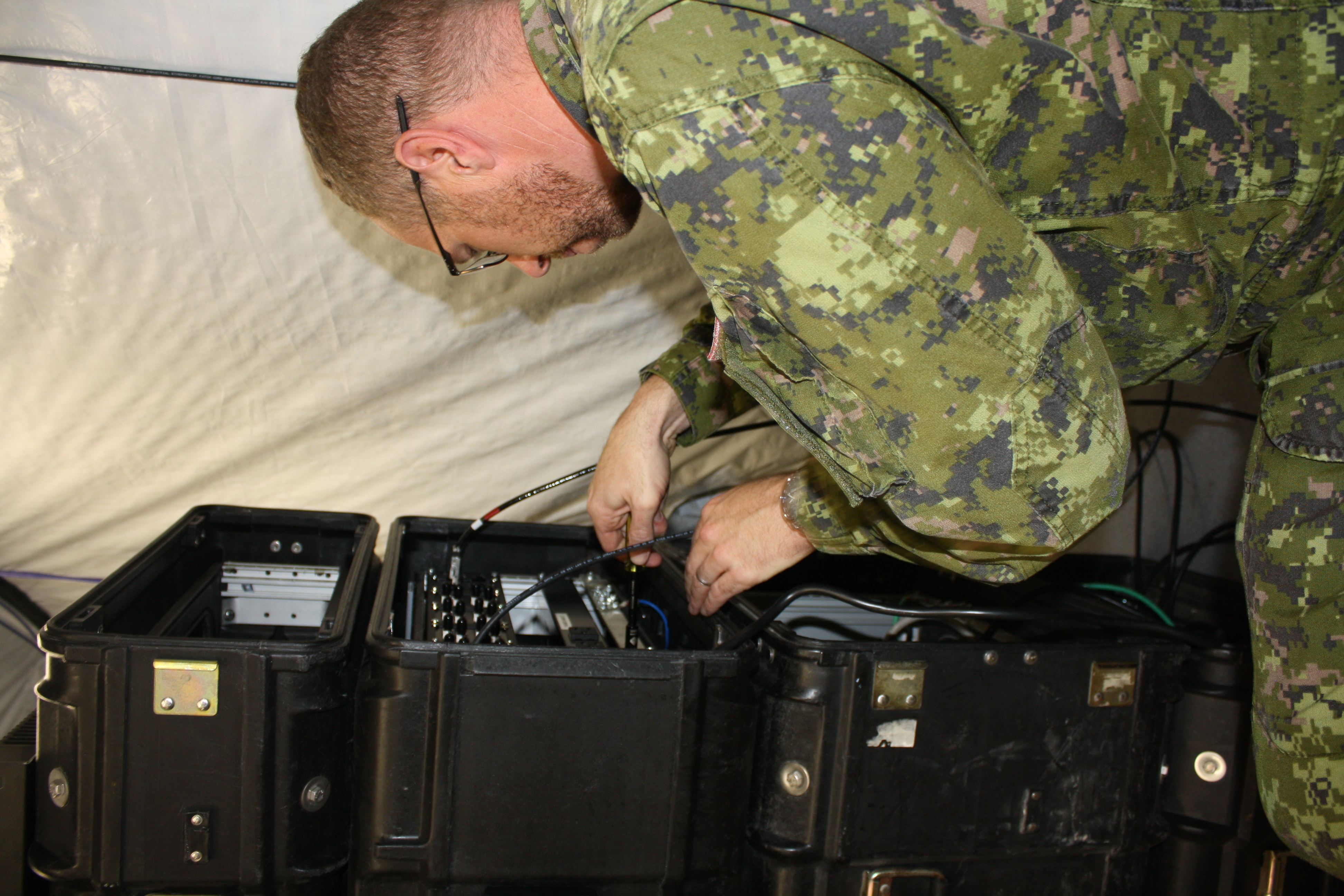 Le caporal-chef Jason Davis, technicien de systèmes d’information et de télécommunications aérospatiales à la 14e Escadre Greenwood, en Nouvelle Écosse, s’affaire à préparer le Centre déployable de soutien de mission de la base en vue d’un entraînement. PHOTO : Sara White