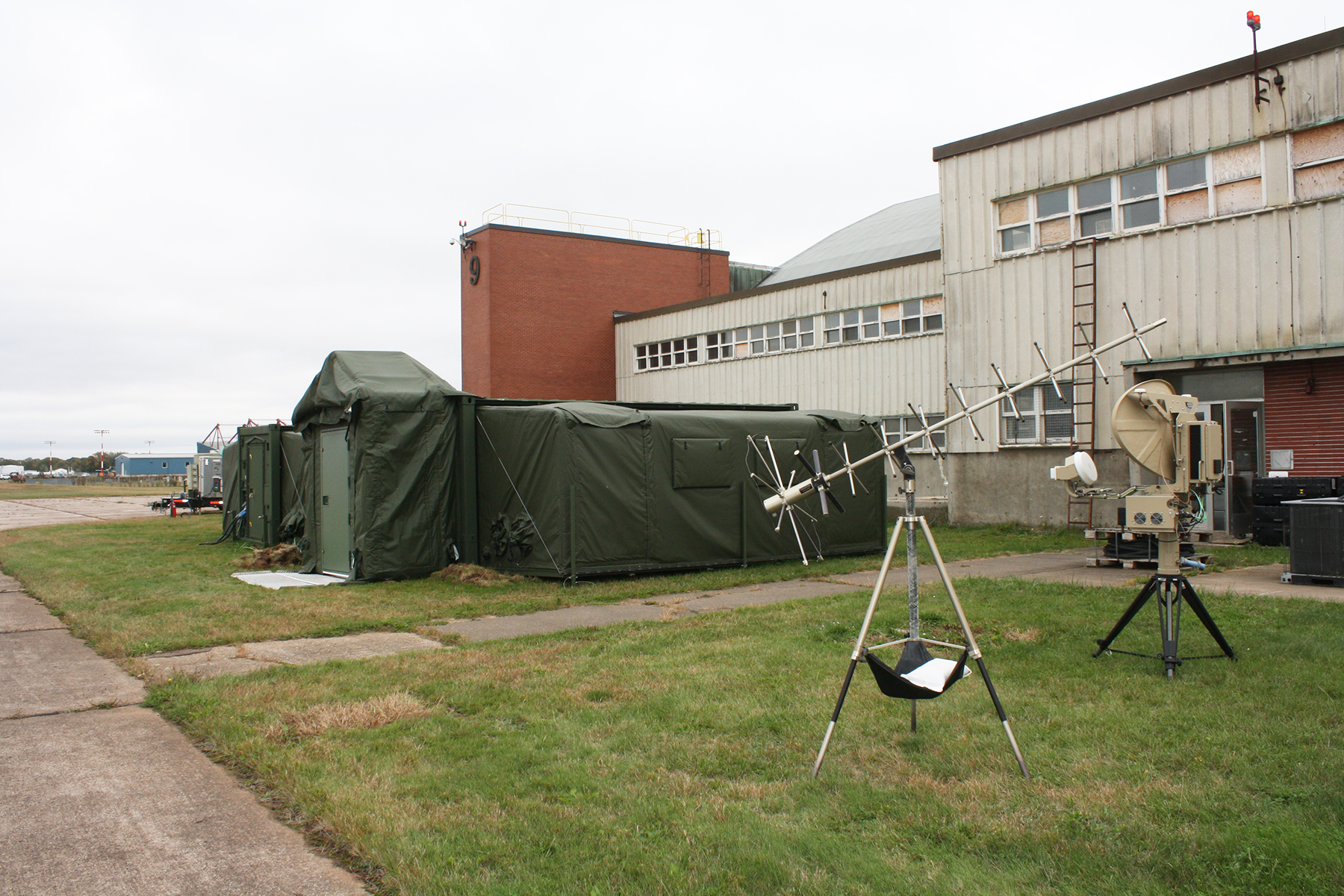 A large olive-green tent sits on the grass alongside a building.