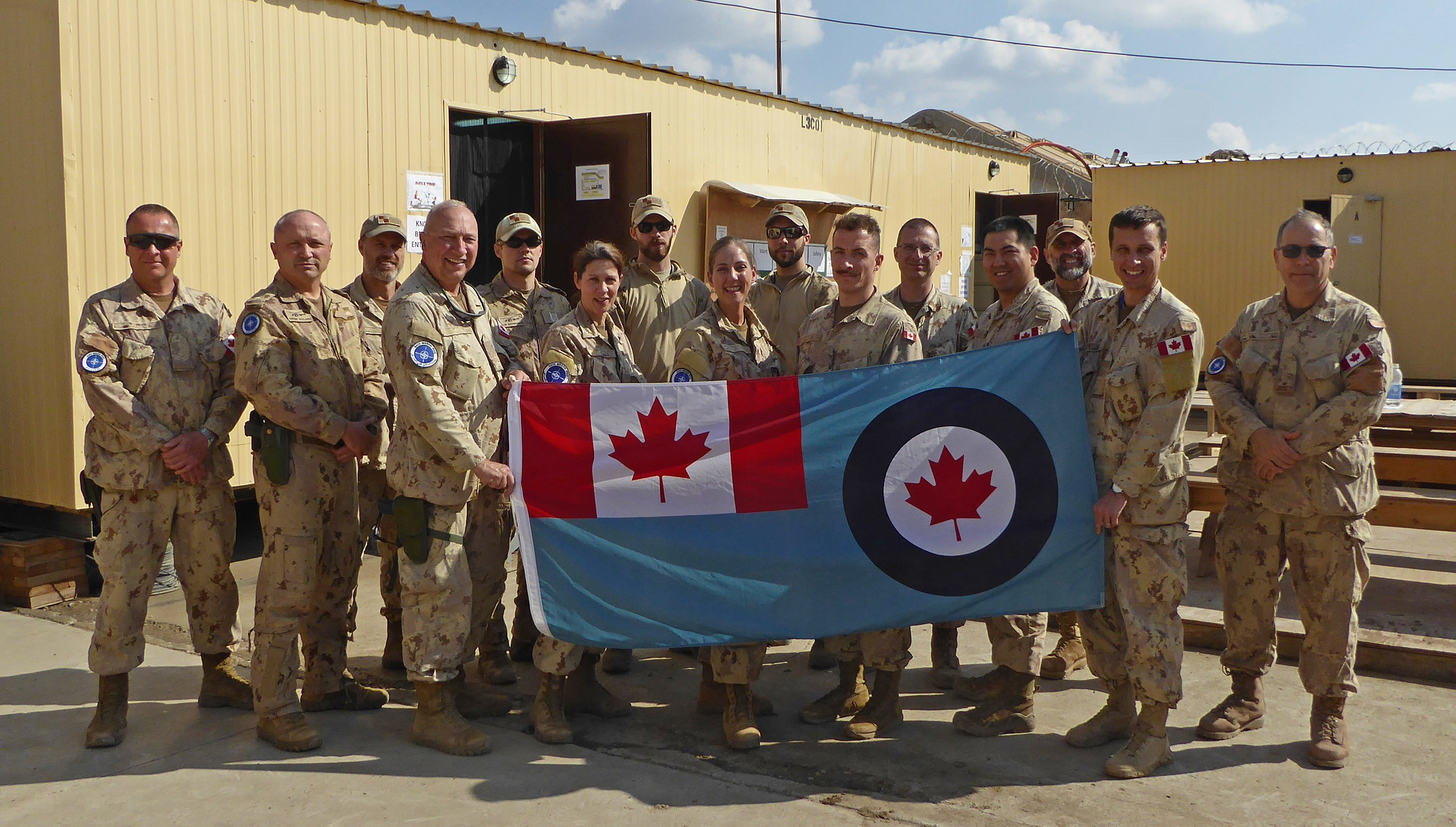 Military personnel hold a large flag.