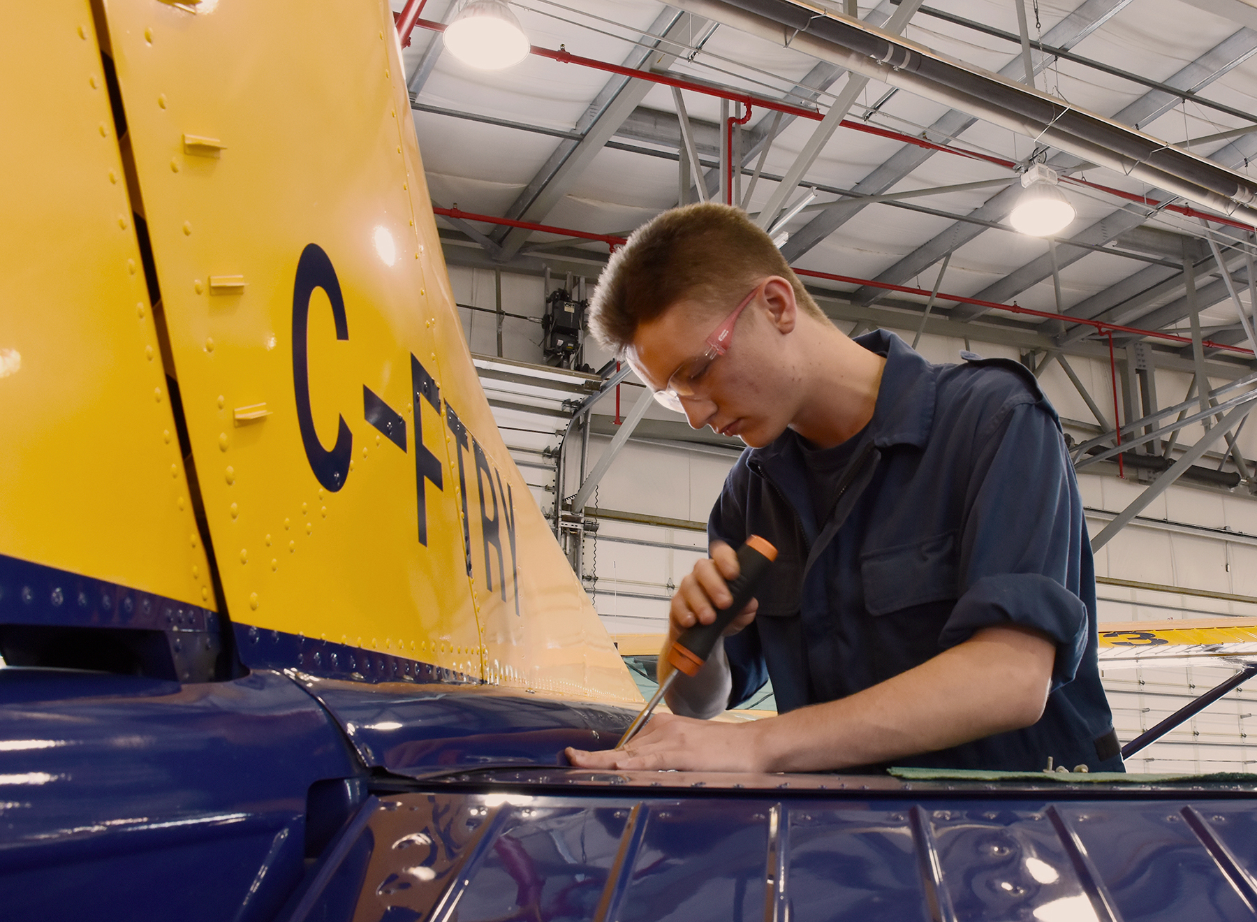 Un jeune homme en combinaison bleu foncé travaille sur la queue d’un aéronef dans un grand bâtiment.
