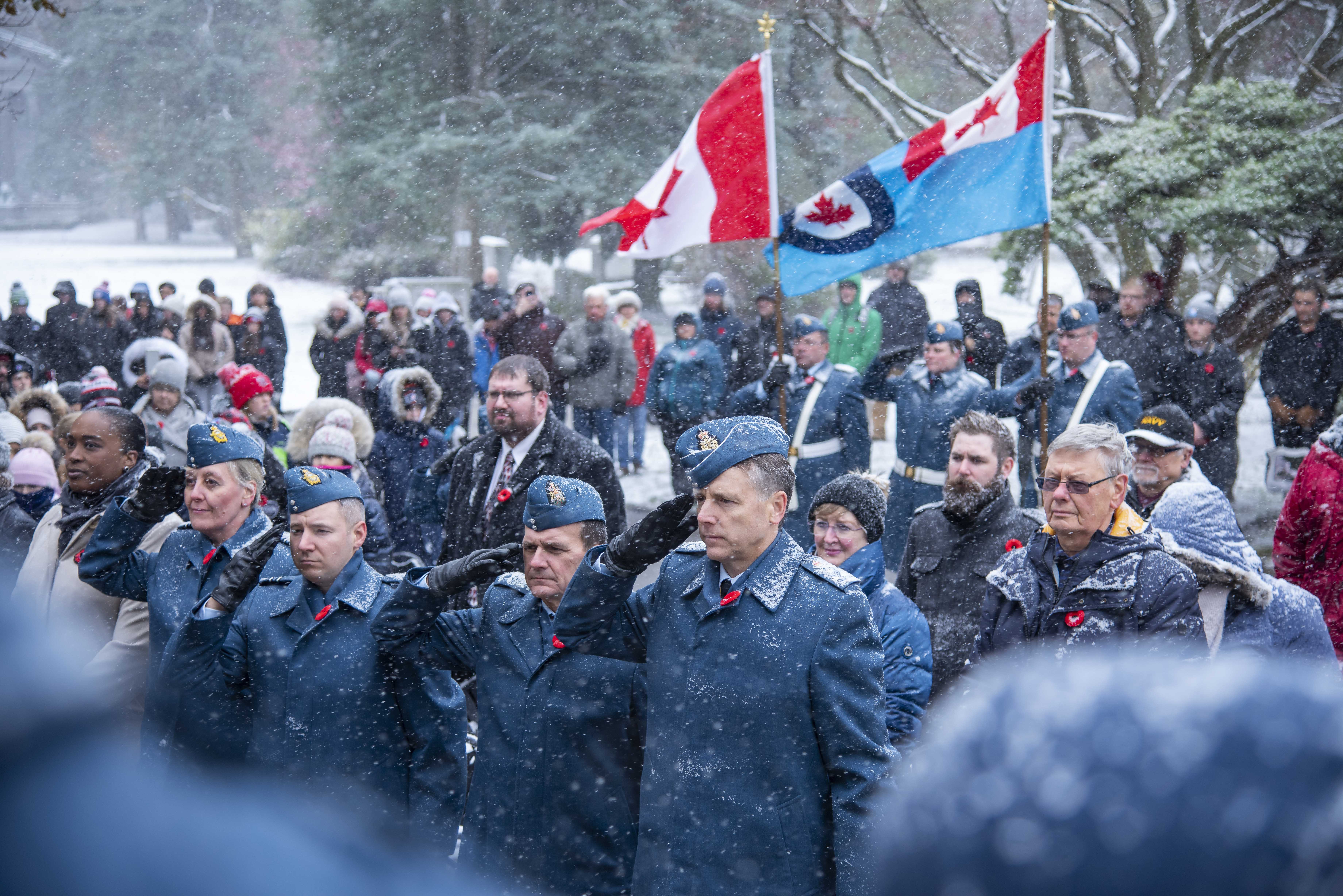 Four people dressed in Air Force uniforms salute, as snow falls. They are surrounded by a crowd of people. 