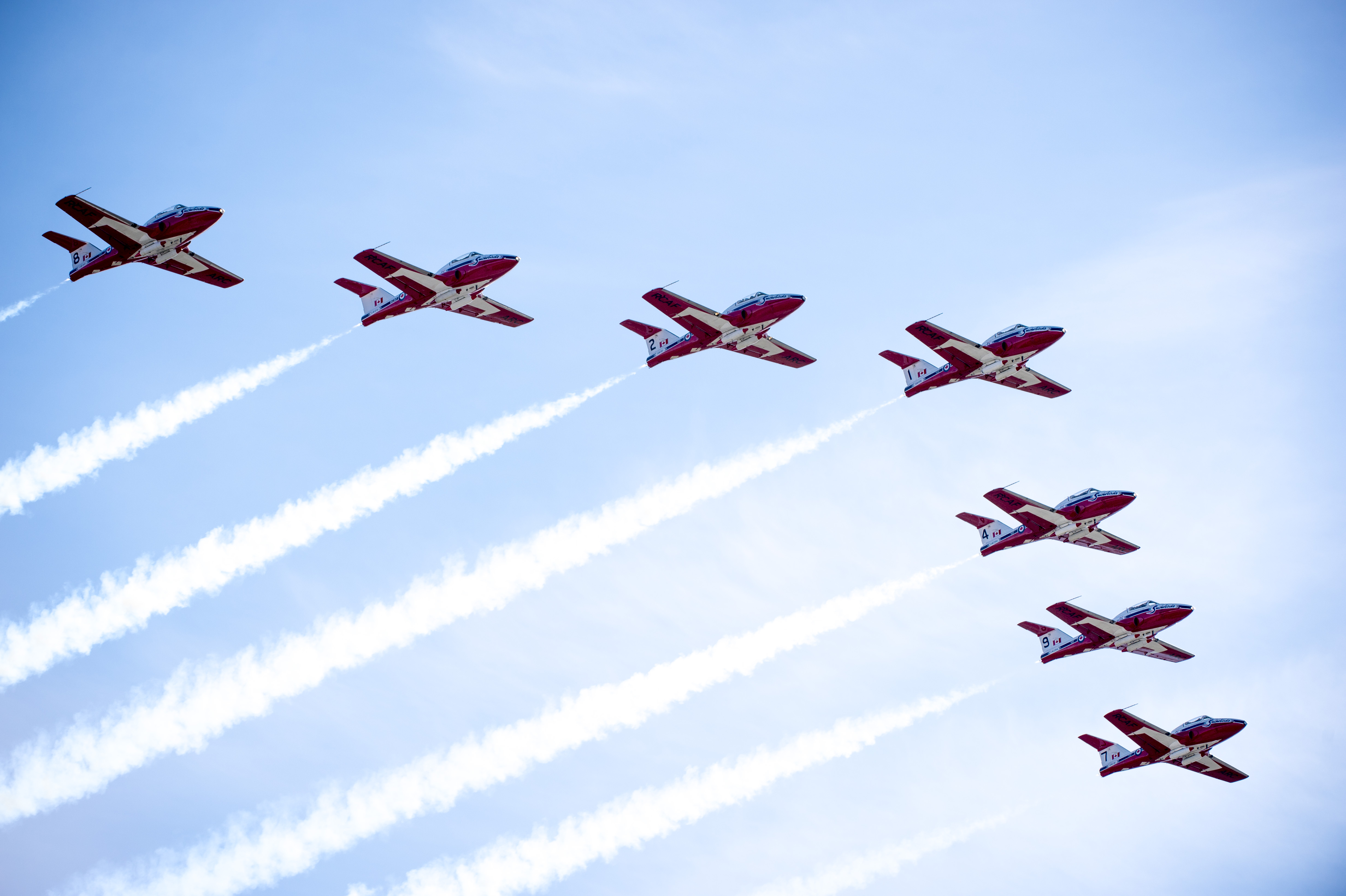 Seven red and white jet aircraft fly in formation.