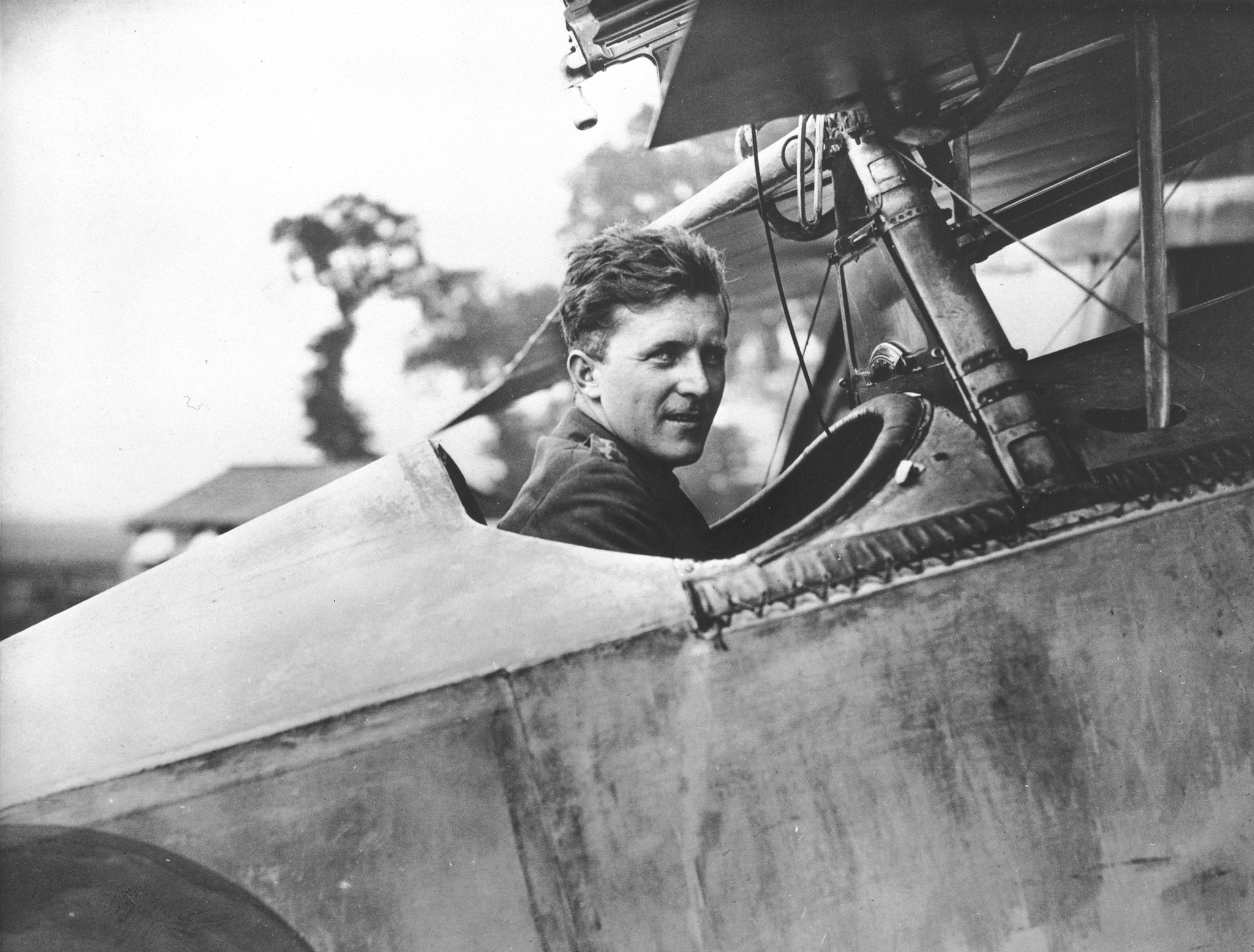 A black and white photo of man sitting in the cockpit of First World War fighter biplane. 