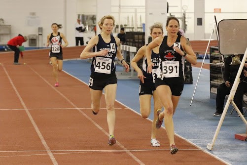 Four women run on a track during a track and field competition.