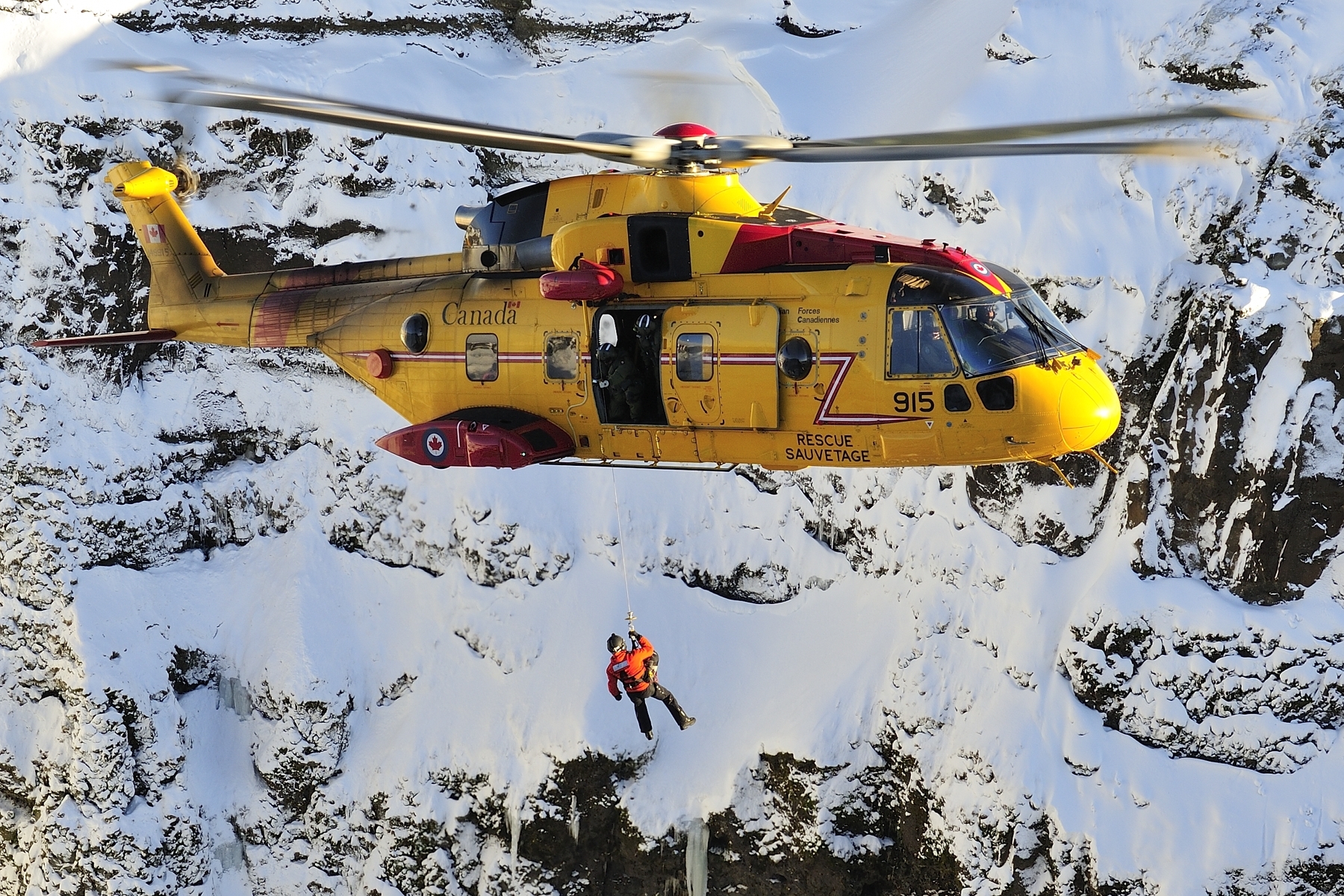 Le sergent Kevin O'Donnell, technicien en recherche et en sauvetage du 103e Escadron de recherche et de sauvetage, basé à Gander, à Terre-Neuve-et-Labrador, descend d’un hélicoptère CH-149 Cormorant à l’aide d’un treuil en vue de participer à un scénario de sauvetage en montagne lors d’un exercice de recherche et de sauvetage en Islande, le 10 février 2016. PHOTO : Caporal-chef Johanie Maheu