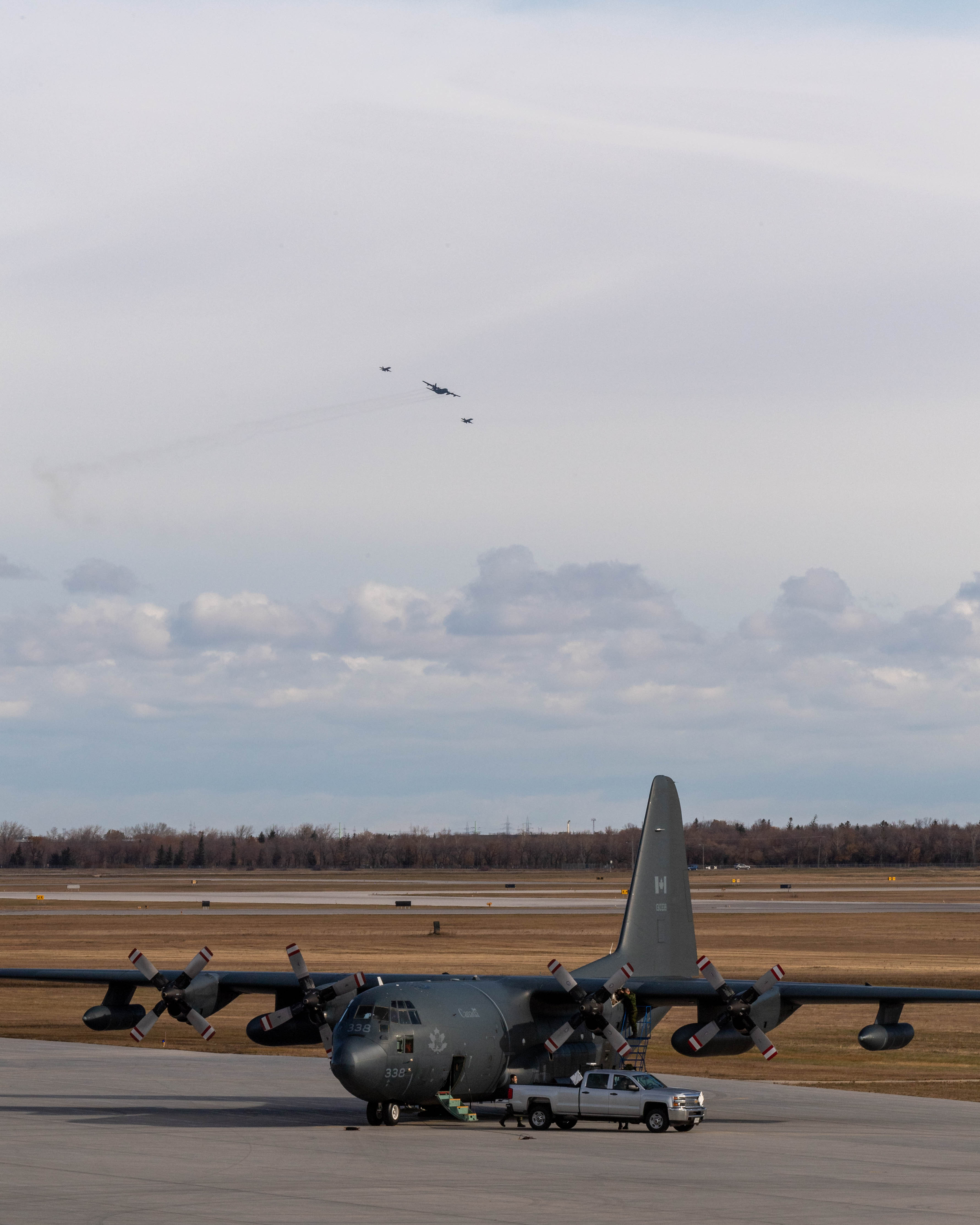 Un avion CC-130 Hercules se trouve sur la piste à la 17e Escadre Winnipeg, au Manitoba, le 13 octobre 2020, alors qu’un autre Hercules vole en formation avec deux chasseurs CF-188 Hornet afin de marquer la 60e année de service de l’aéronef dans l’Aviation royale canadienne. PHOTO : Caporal Darryl Hepner