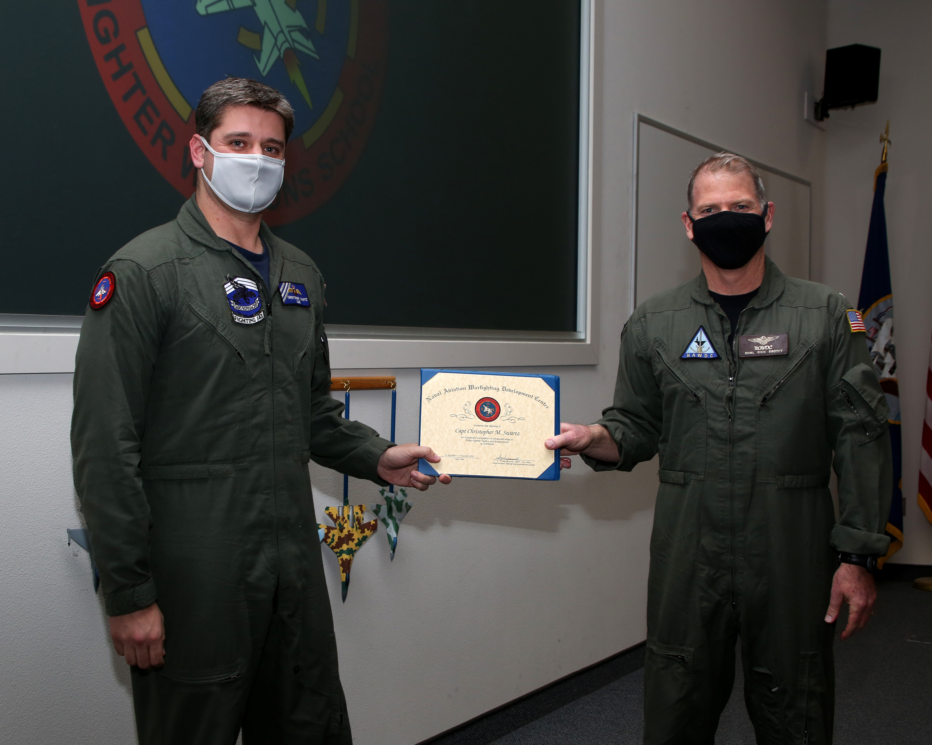 Deux hommes vêtus de combinaisons de vol vertes et portant un masque tiennent ensemble un certificat.