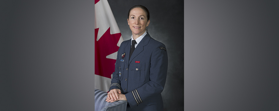 slide - A smiling woman wearing a blue military uniform stands in front of a Canadian flag, her hands resting on a blue chair.
