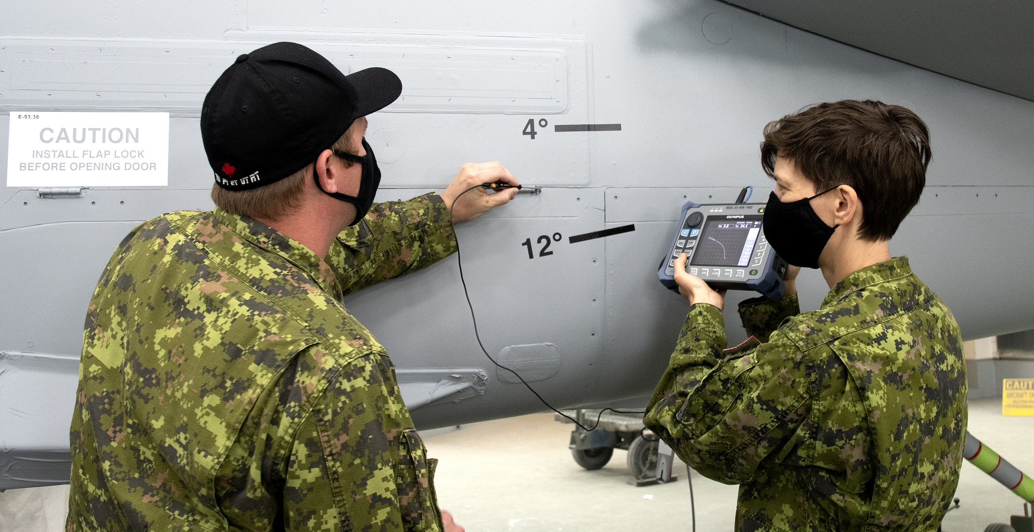 Non-destructive testing technicians Corporal Eddy Ford (left) from 8 AMS, and Corporal Maggie Selley (right), from ATESS, inspect the fuselage of a CF-18 Hornet for cracks in the skin (surface) using eddy current testing techniques.  