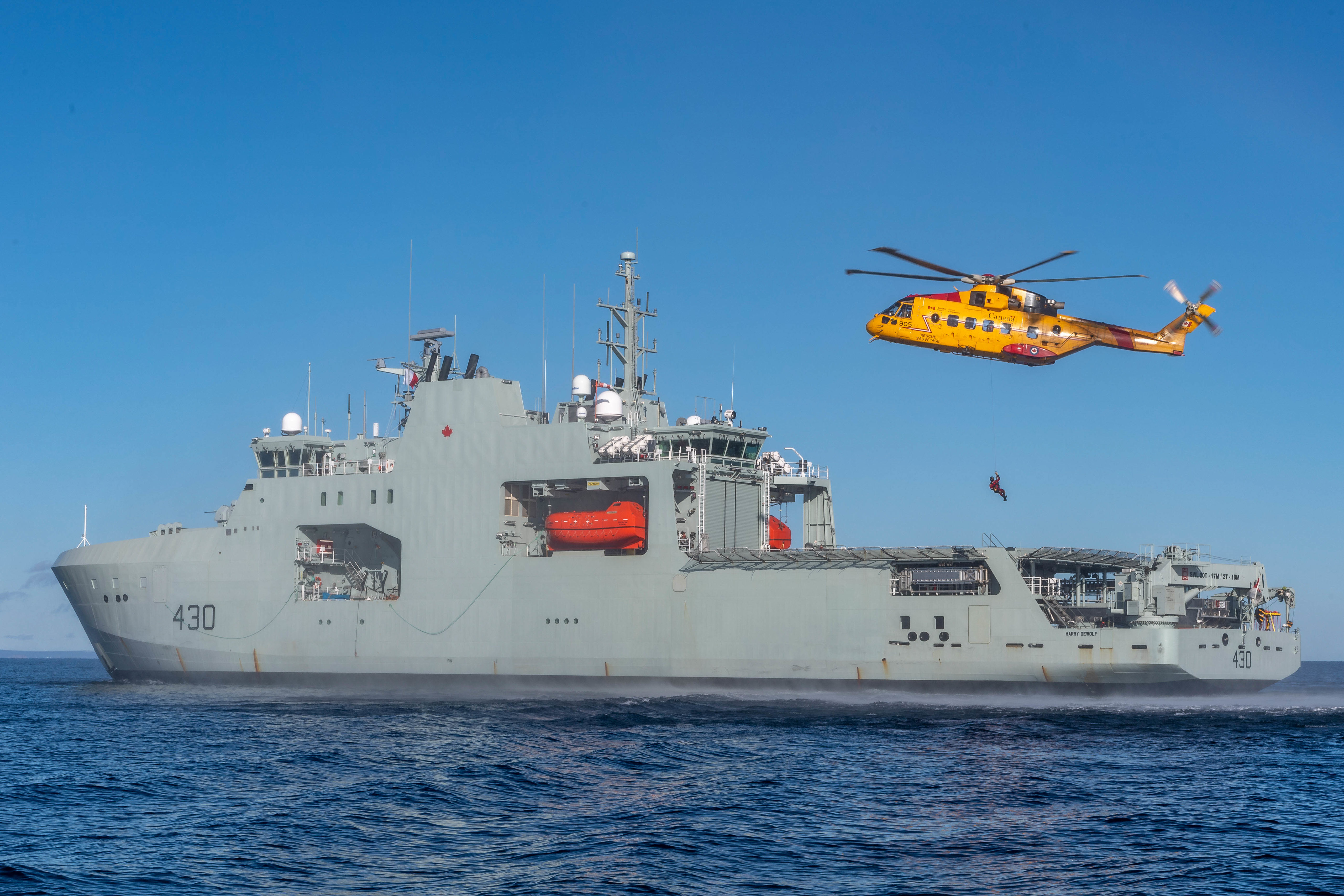 A CH-149 Cormorant helicopter lowers a Search and Rescue Technician aboard HMCS Harry DeWolf