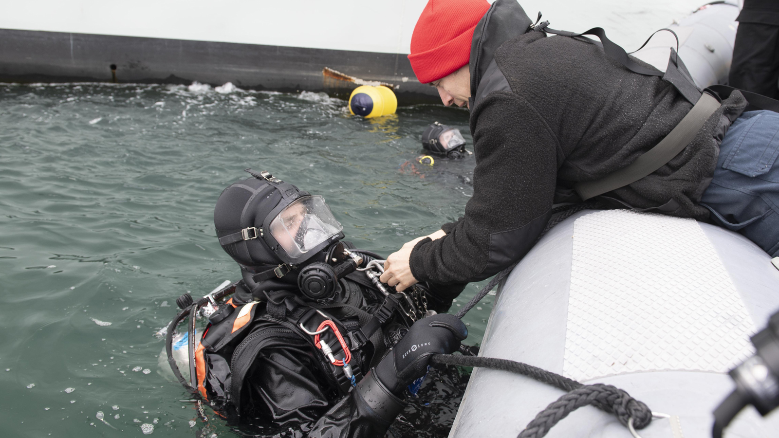 Le matelot de 1re classe (mat 1) Cory Taylor (à droite) aide le Mat 1 John Kester à retirer son équipement à la fin d’une opération de plongée au port de Reykjavik, en Islande.