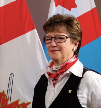 Photographie de la vétérante Suzie Bouchard devant des drapeaux canadiens.