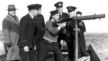 Des marins et des officiers de la Marine entourent un canon installé à bord d’un navire de la Marine.